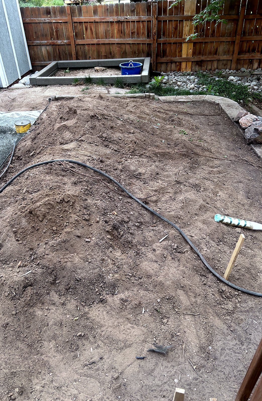 Backyard stripped to bare soil and regraded, hose and stakes set for layout