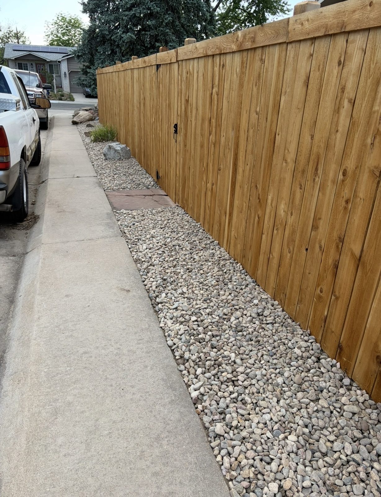 Long cedar privacy fence run with a rock border beside a sidewalk