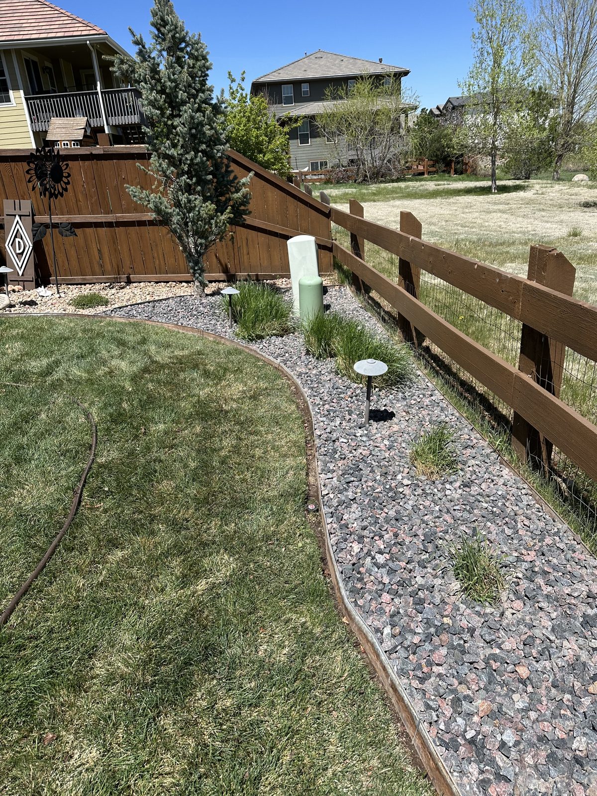 Curved rock bed with ornamental grasses and path lighting along a split-rail fence