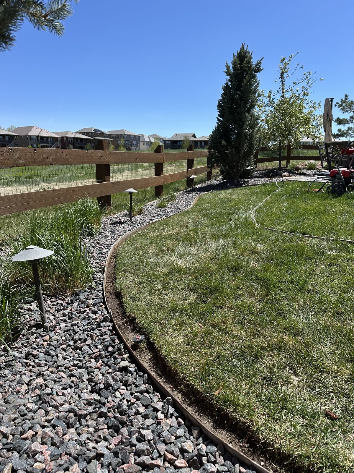 Curved steel edging separating lawn from a rock bed with low-voltage path lights
